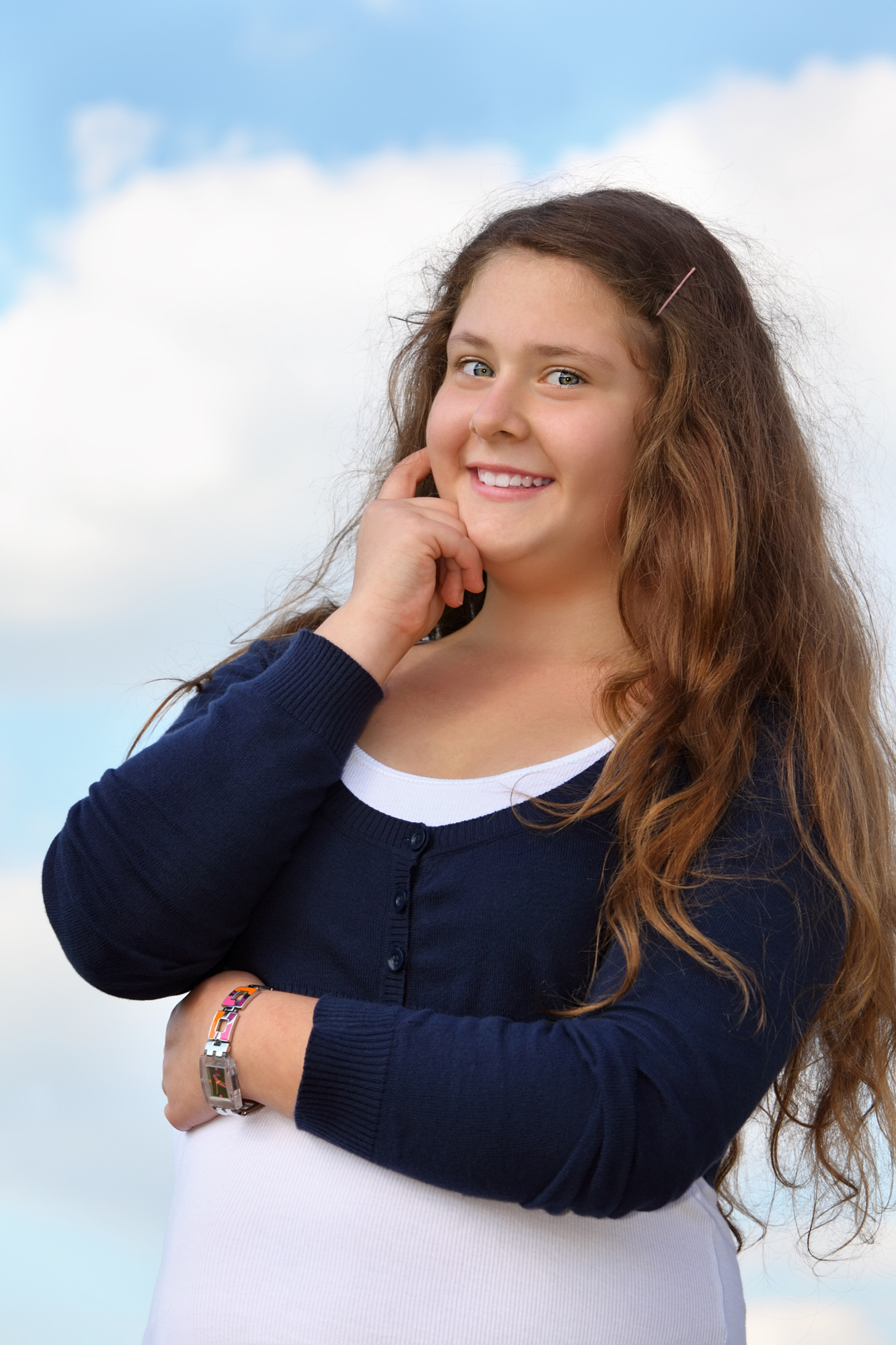 Beautiful smiling girl looks at camera at background of blue sky with clouds.