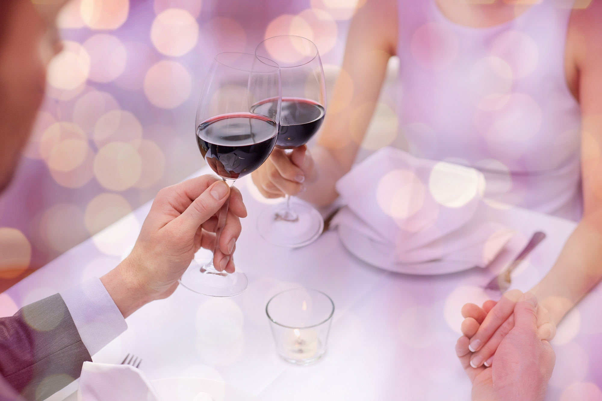 restaurant, people, celebration and holiday concept - close up of young couple with glasses of red wine at restaurant over violet holidays lights background