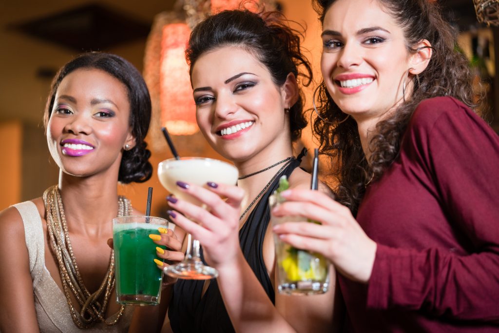 Beautiful girls in nightlife drinking cocktails and saying Cheers