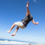 Teen boy jumping off wall into summersault flips on beach
